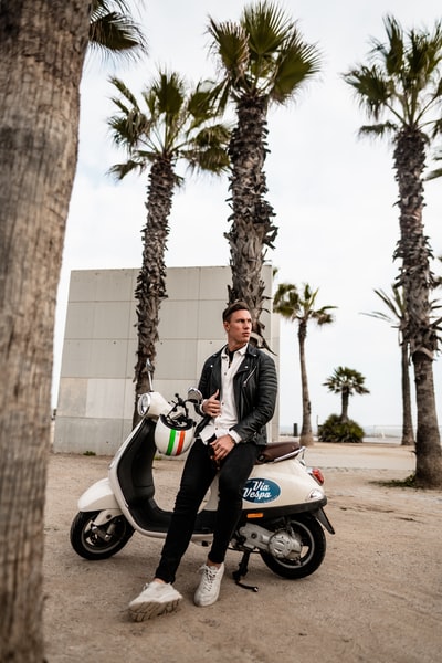 A man was sitting on the motorcycle parking beside a tree
